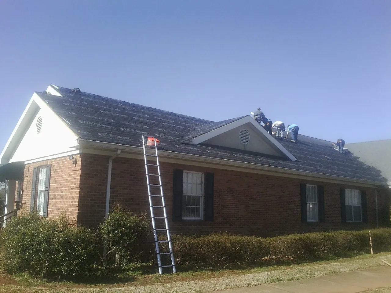 Crew tearing shingles off a brick ranch roof with a ladder set — Metal Roof Repair work by our crew in Gaithersburg