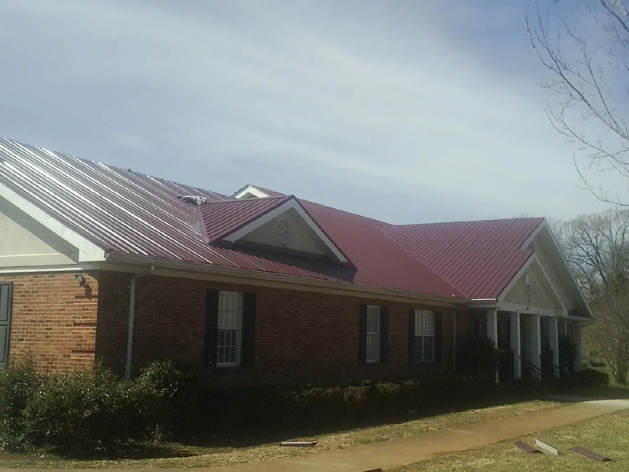 Red metal roof with gabled entries on a long brick building, from a Hail Damage Roof Repair job in Gaithersburg