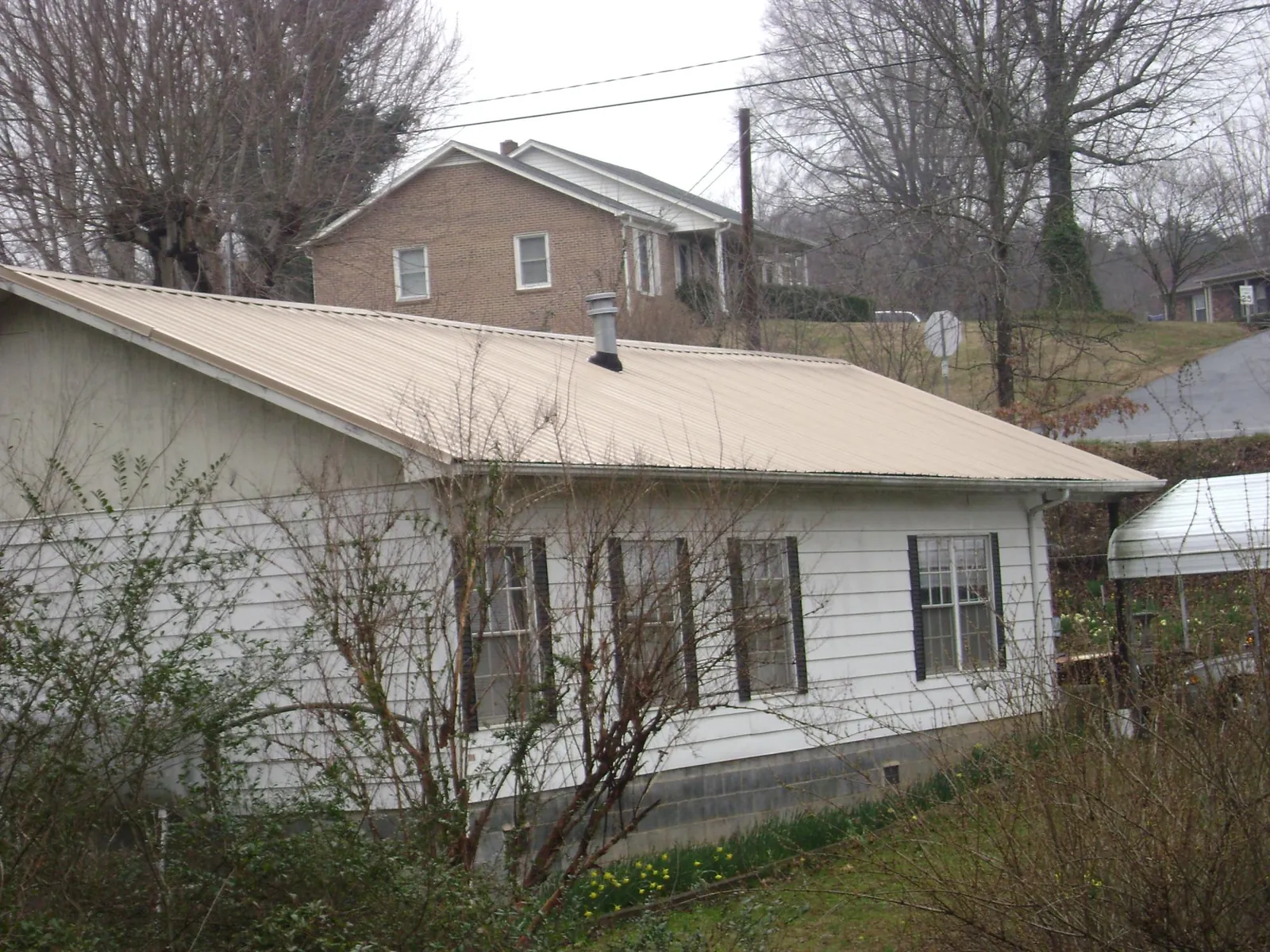 Tan metal roof on a white sided house set into a hillside — Commercial Roofing by Roofing Brothers in Gaithersburg